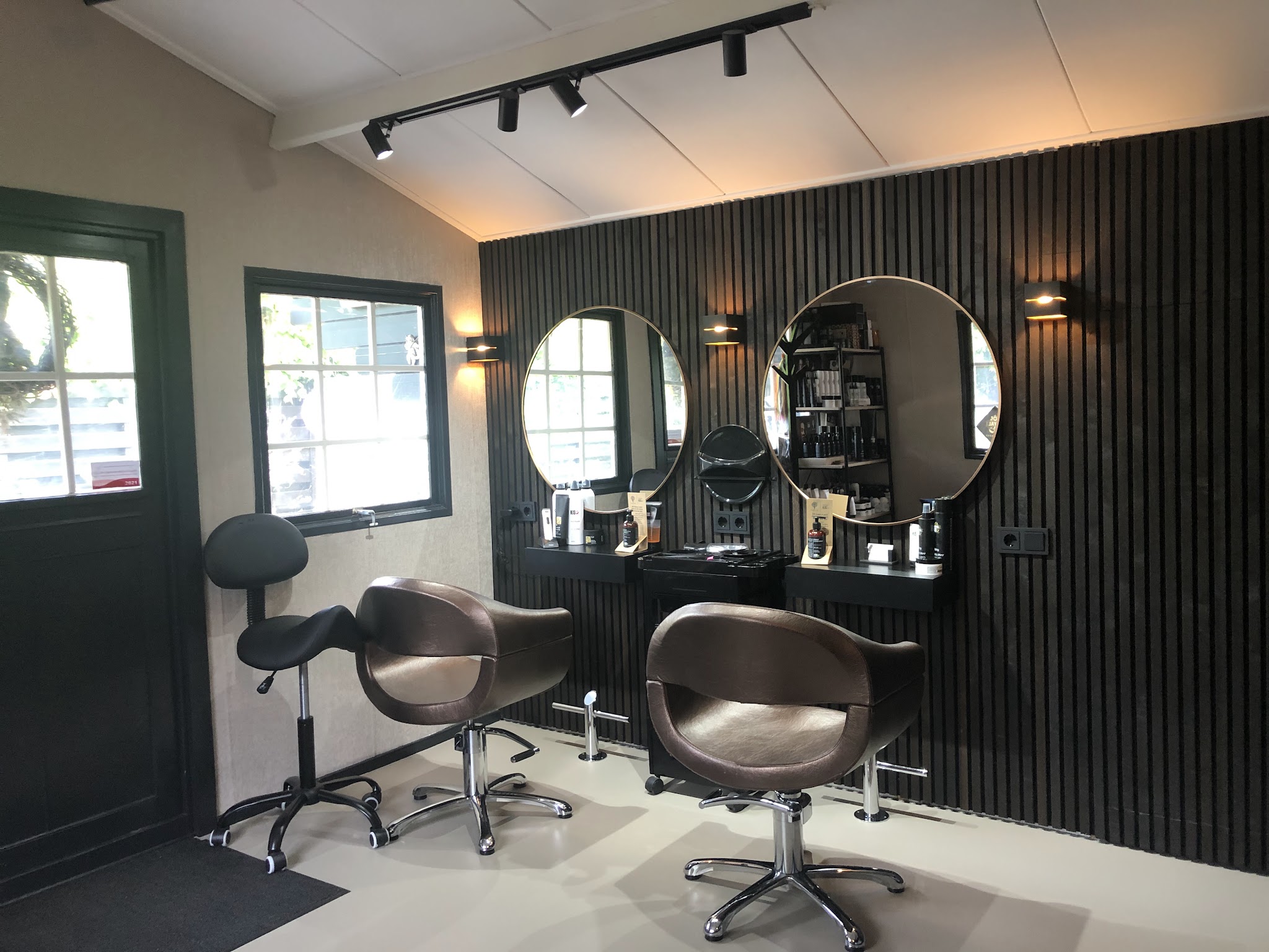 De salon van binnen: twee stoelen, ronde spiegels met messing rand en een zwarte lattenwand